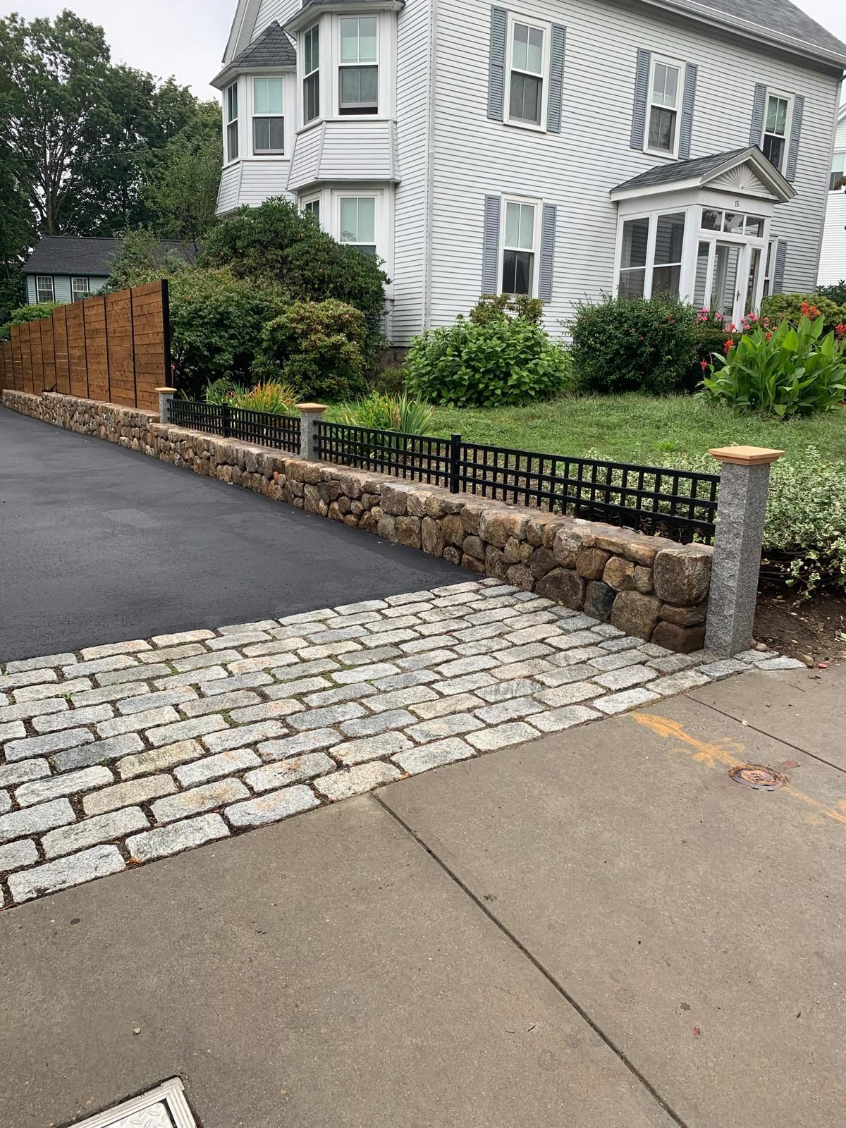 Sidewalk and driveway with cobblestones beside a white house and stone retaining wall