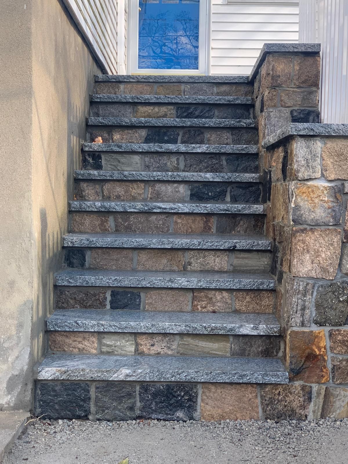 Stone front steps leading to a house entrance with white siding and stone retaining walls