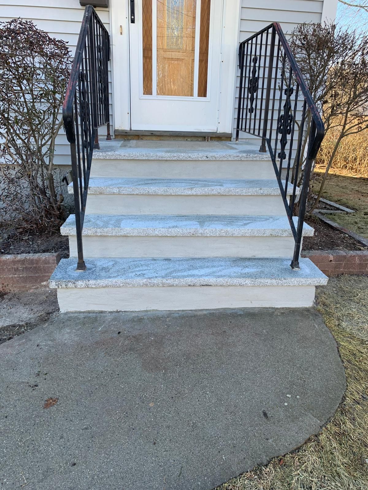 Front steps with black railings leading to a white door, with a curved concrete walkway and grass beside it