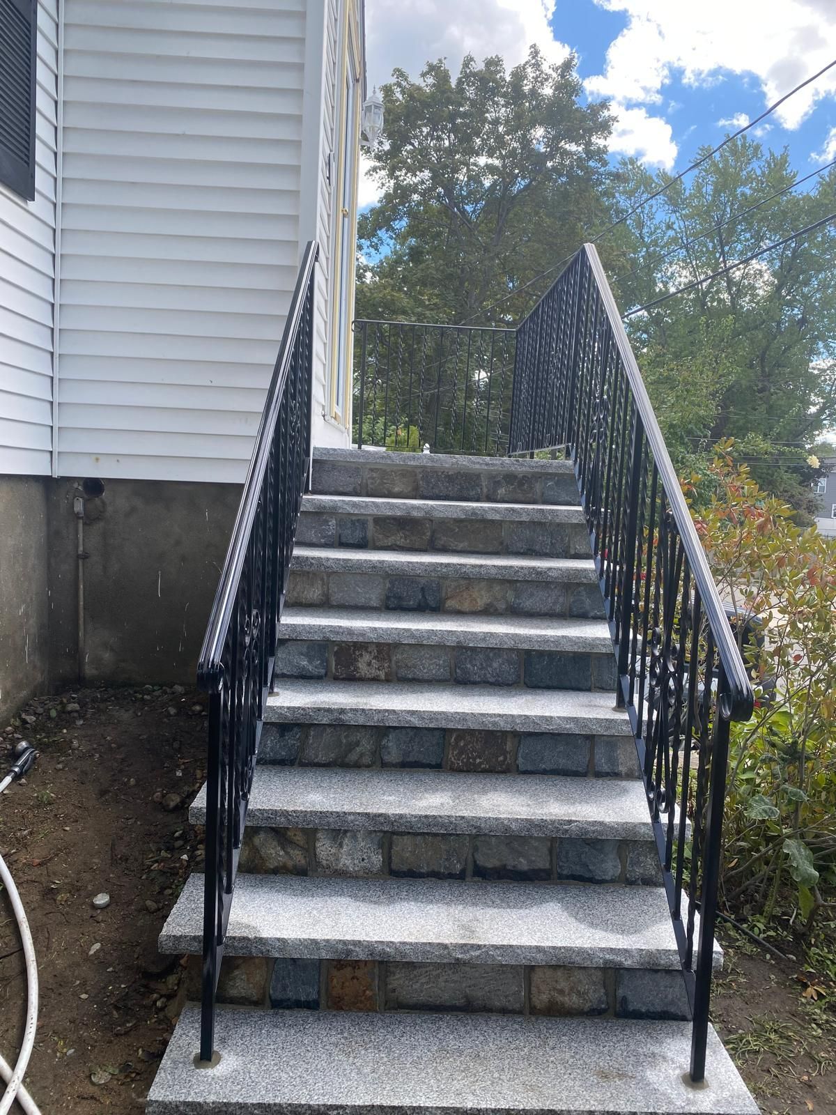 Outdoor concrete stairs with black metal railings beside a house, leading up a small slope