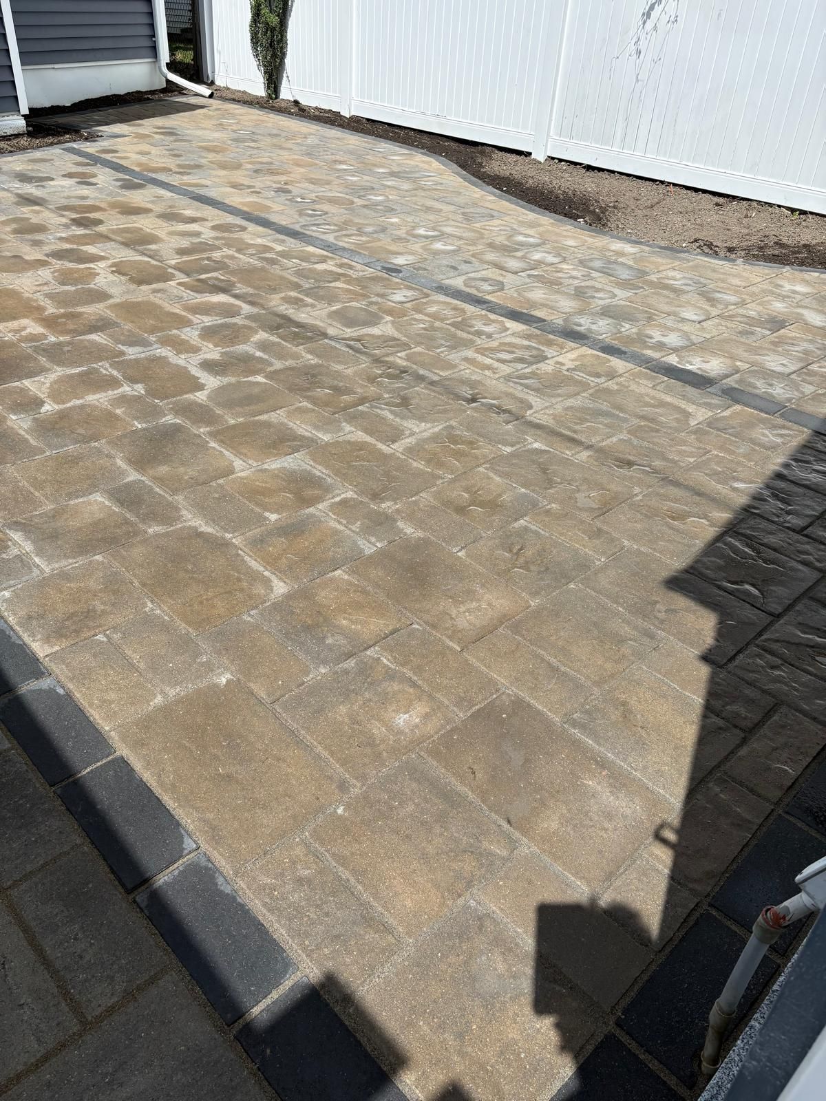 Sunlit stone patio with brick pavers beside white walls and a dark shadow in the foreground