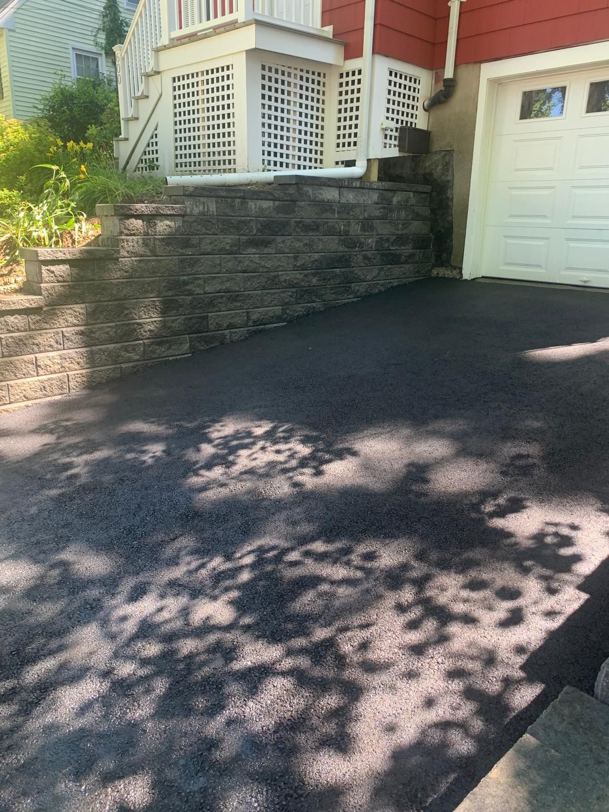 Asphalt driveway beside stone retaining wall and garage with white door in front of a house