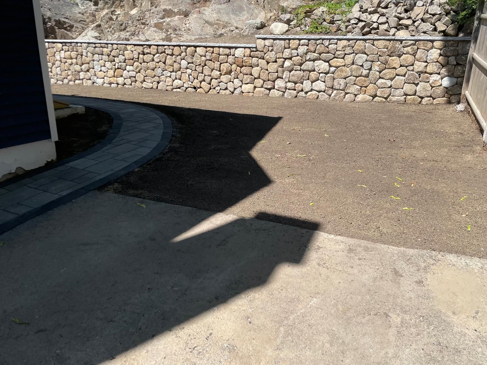 Sunlit paved walkway beside a stone retaining wall, with sharp building shadows across the ground
