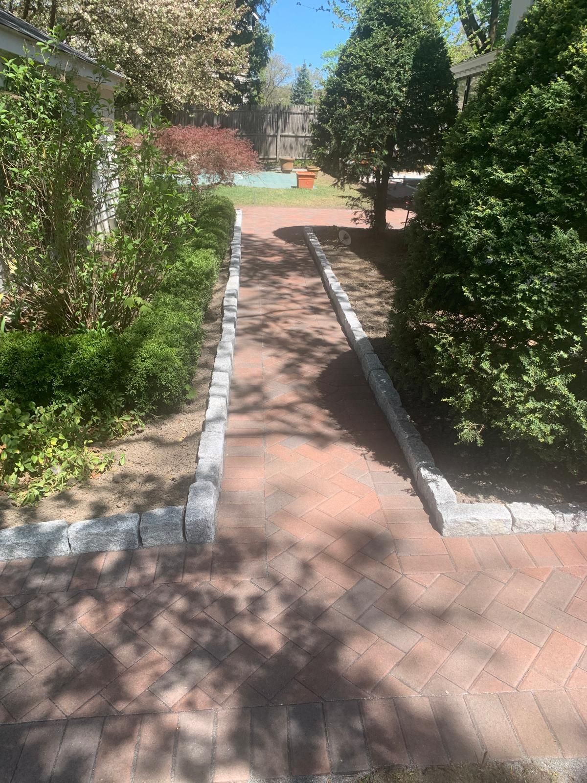 Brick walkway between green hedges leading to a sunlit courtyard garden