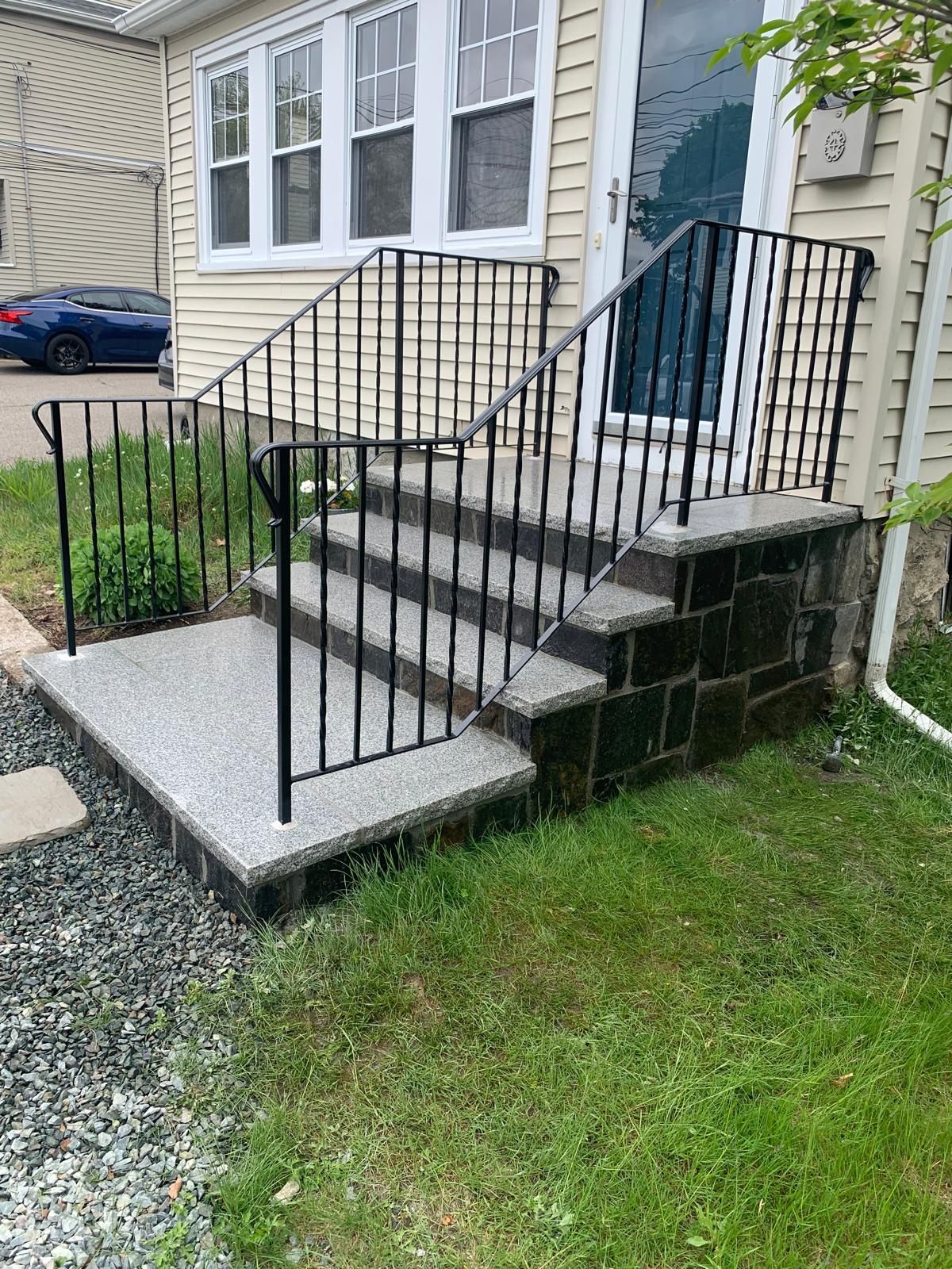 Front steps with black metal railings leading to a house entrance and small concrete landing.