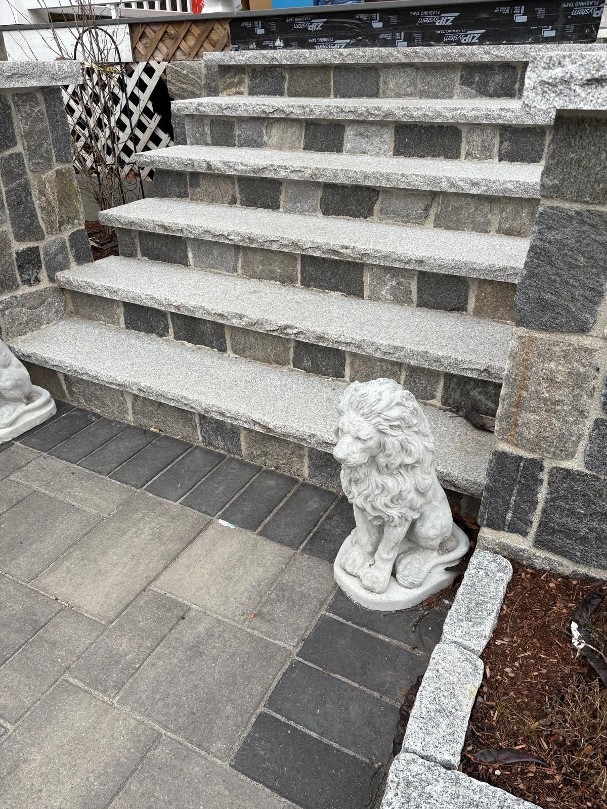 Stone steps leading to a porch, flanked by decorative lion statues and gray pavers
