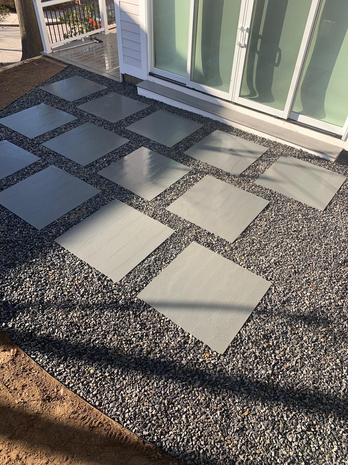 Gravel patio with square stepping stones beside a sliding glass door, sunlit with long shadows
