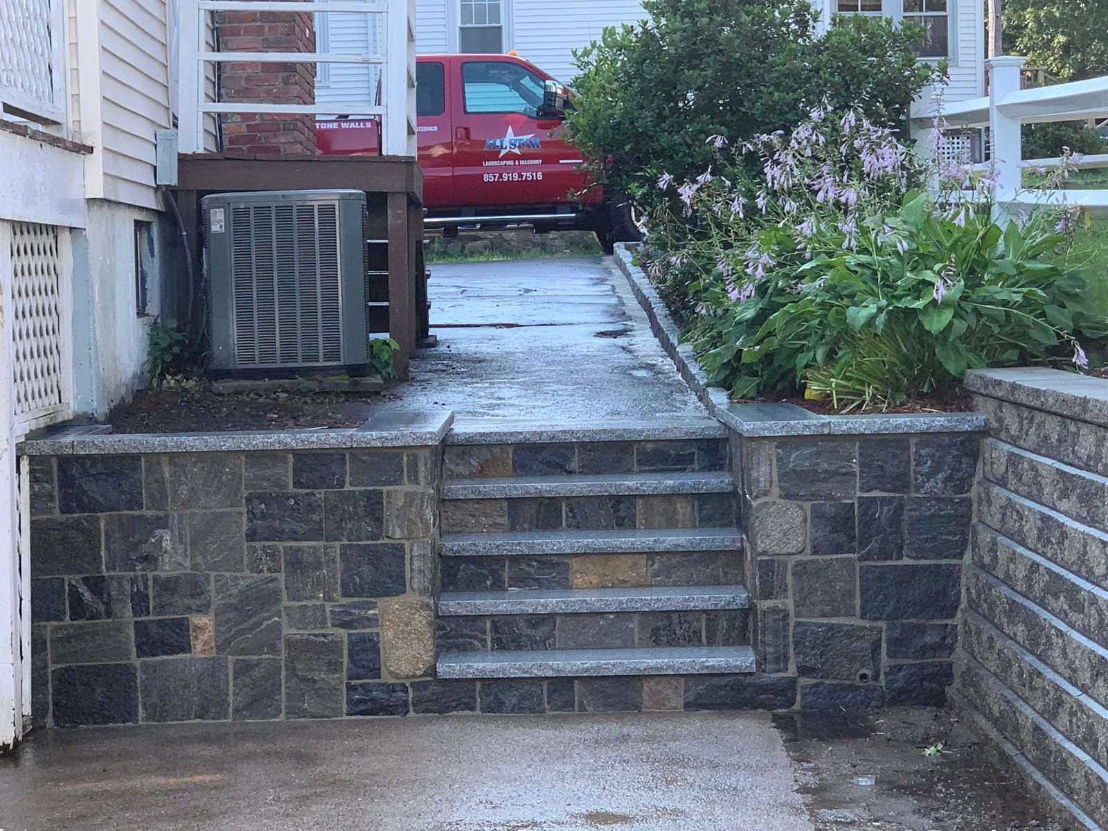 Stone steps leading up to a red car parked beside a house and garden greenery.