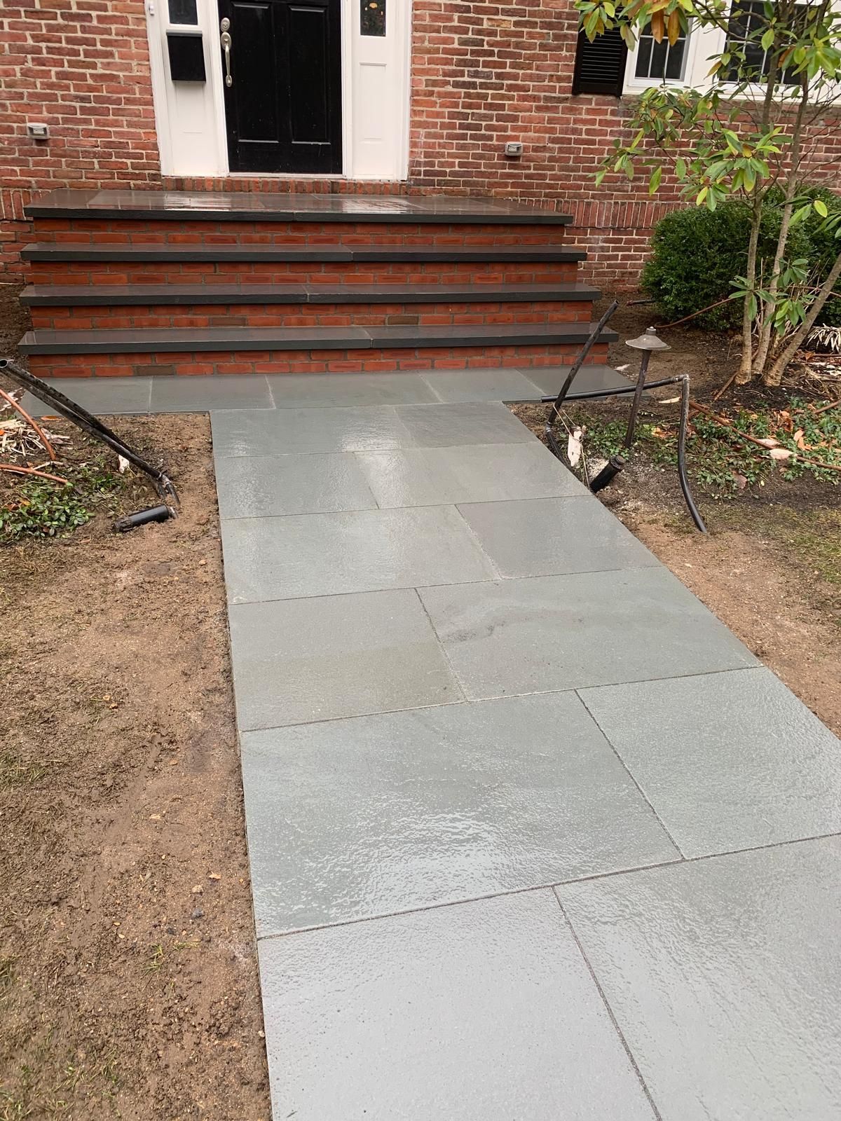Front walkway leading to brick house steps and open doorway, with a gray concrete ramp in the center