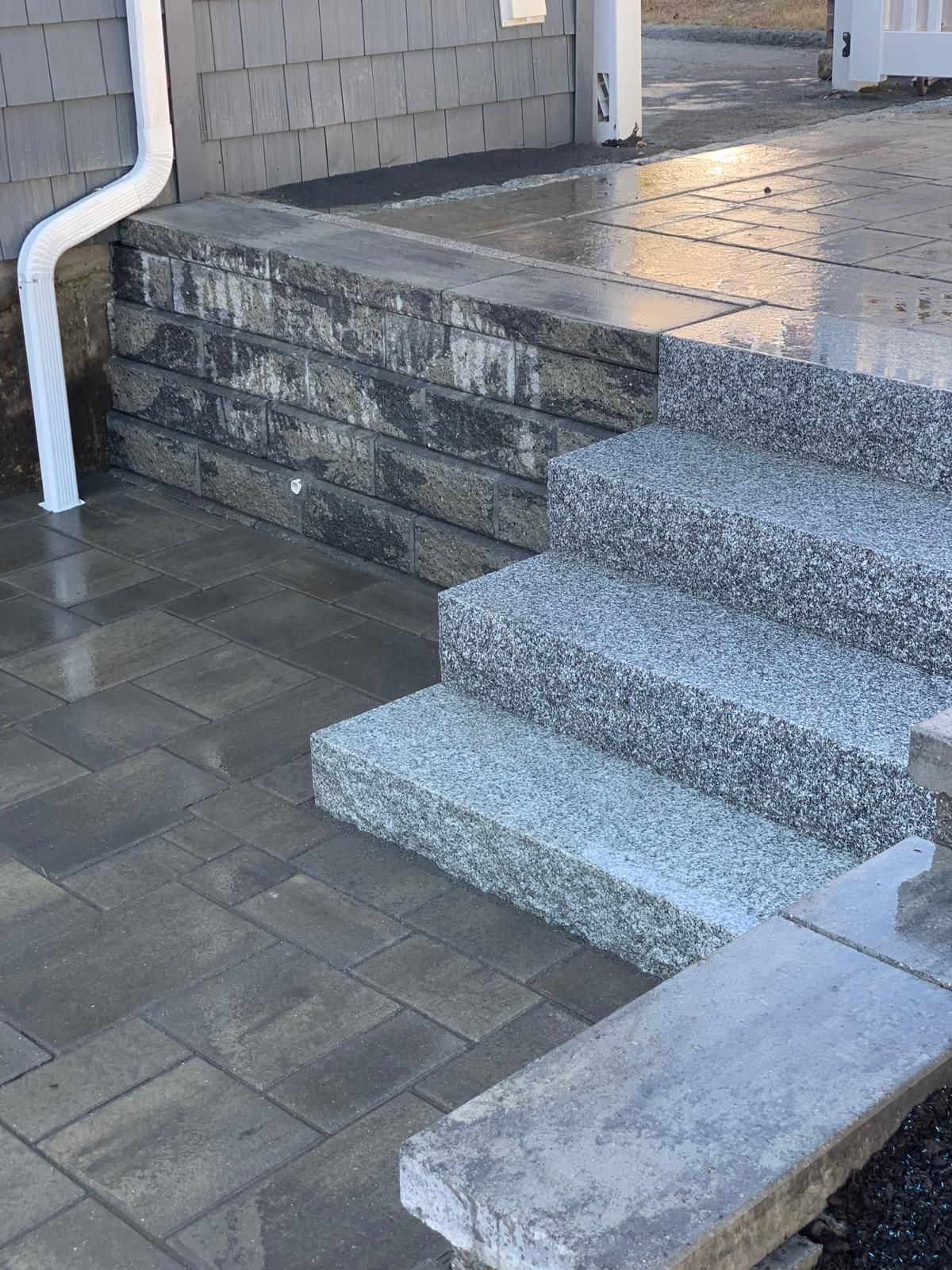 Concrete steps and a ramp leading to a house entrance, with wet pavement and a white railing