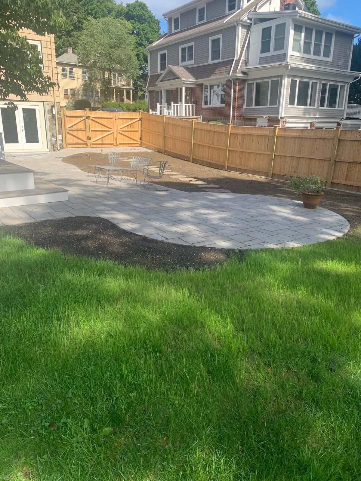 Backyard with green lawn, paved patio, wooden fence, and a house in the background