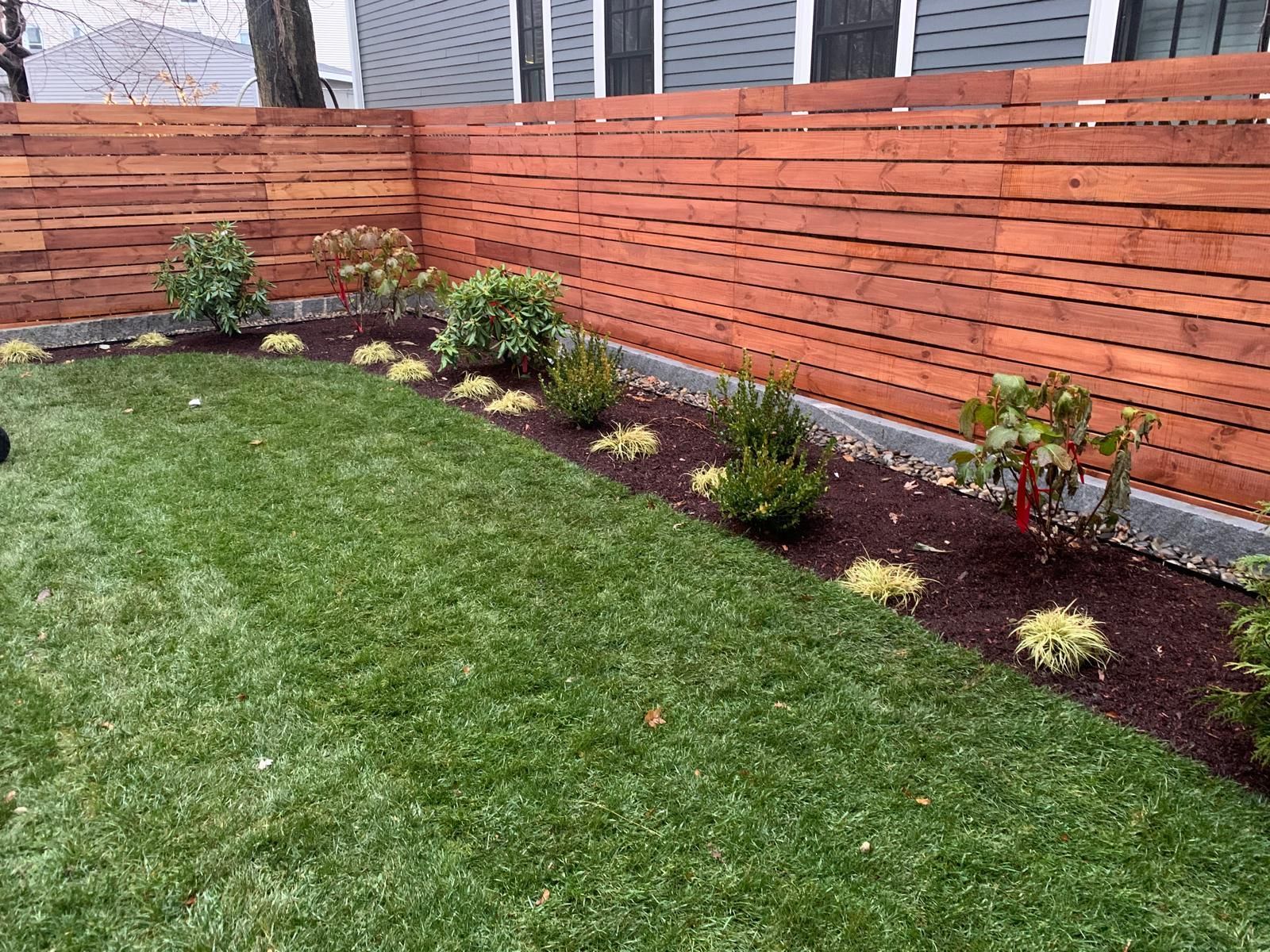 Backyard with green lawn, wooden privacy fence, and a mulched garden bed with shrubs