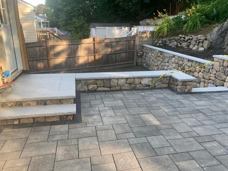 Stone patio and steps leading to a wooden gate, with low stone retaining walls and paved courtyard.