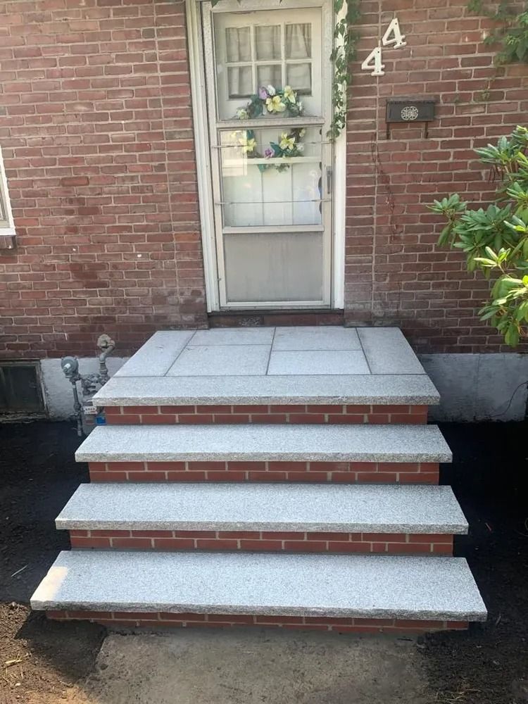 Brick house front steps with three concrete stairs and a white screen door