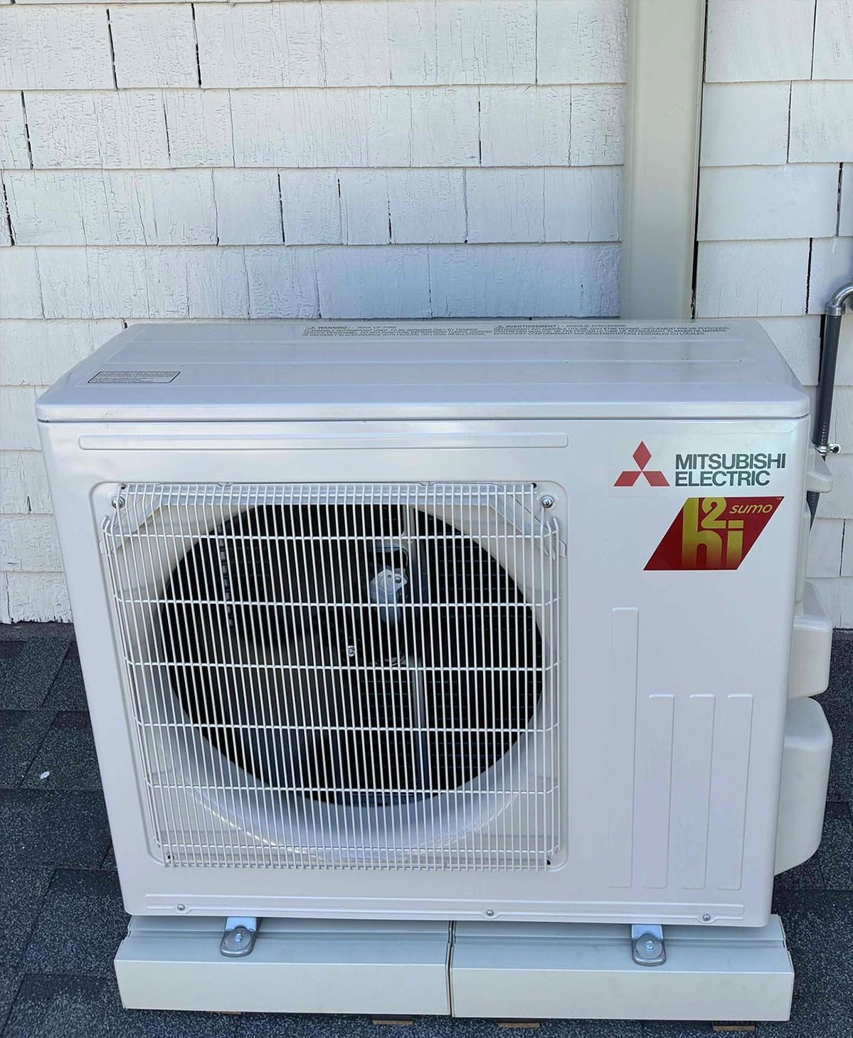 White Mitsubishi air conditioner outdoor unit beside a brick wall