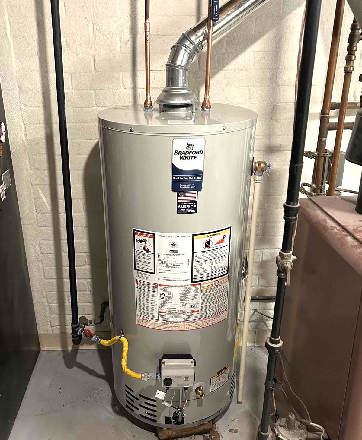 Gray water heater in a utility room with visible pipes and yellow gas line