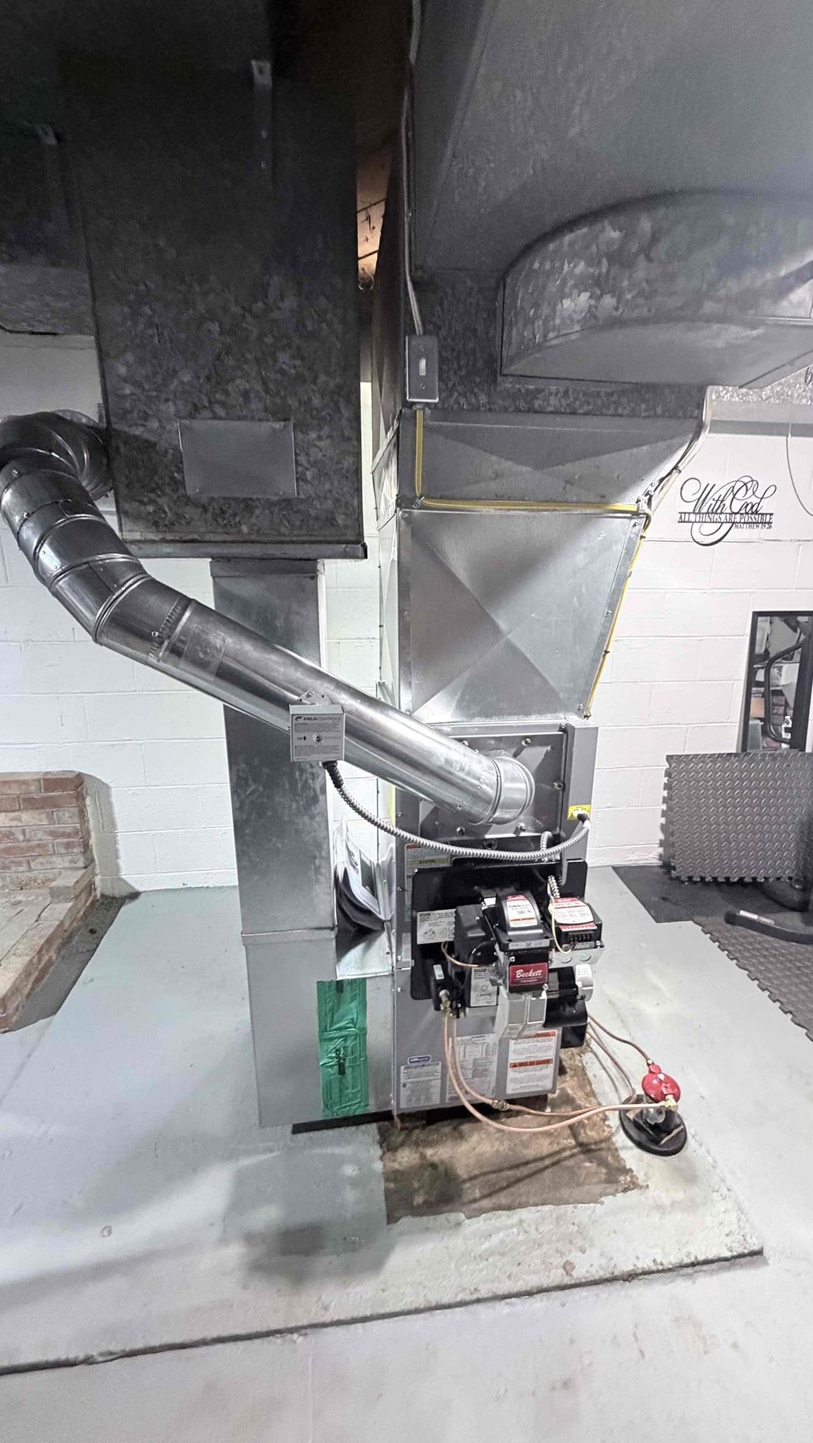 Metal ductwork and HVAC equipment in a utility room with a white wall and concrete floor.