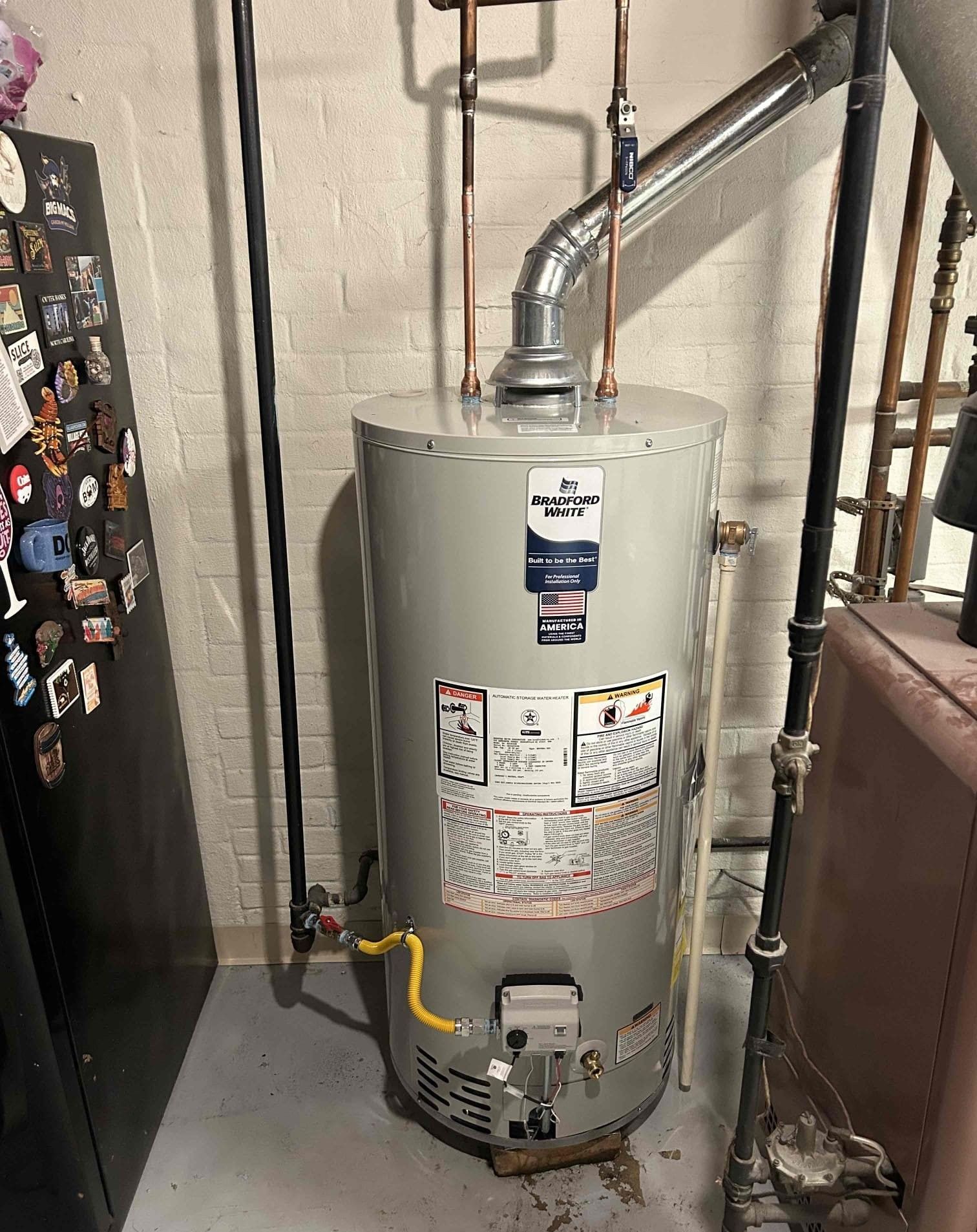 Water heater in a utility closet with exposed pipes and warning labels.