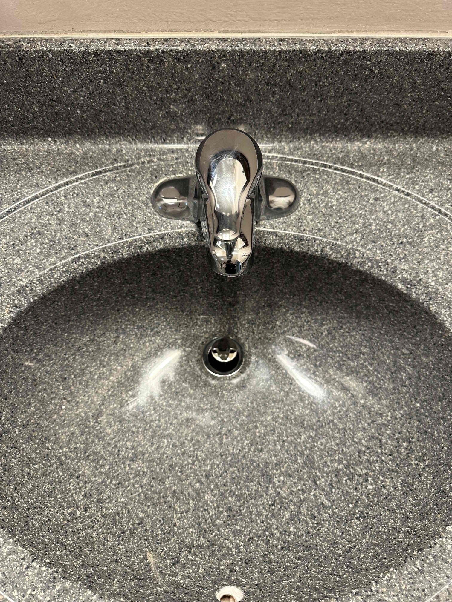 Chrome bathroom sink with faucet and speckled countertop reflected in the basin