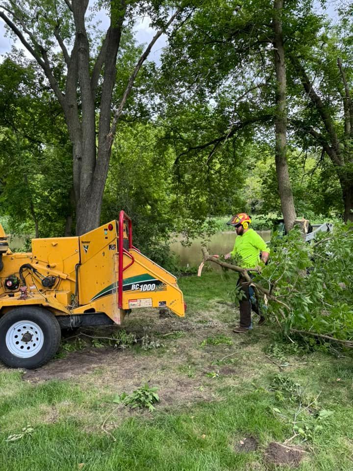 A man is standing next to a tree chipper in a field.