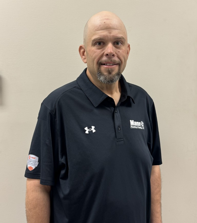 Man with a shaved head and goatee in a black polo shirt, standing in front of a neutral wall.
