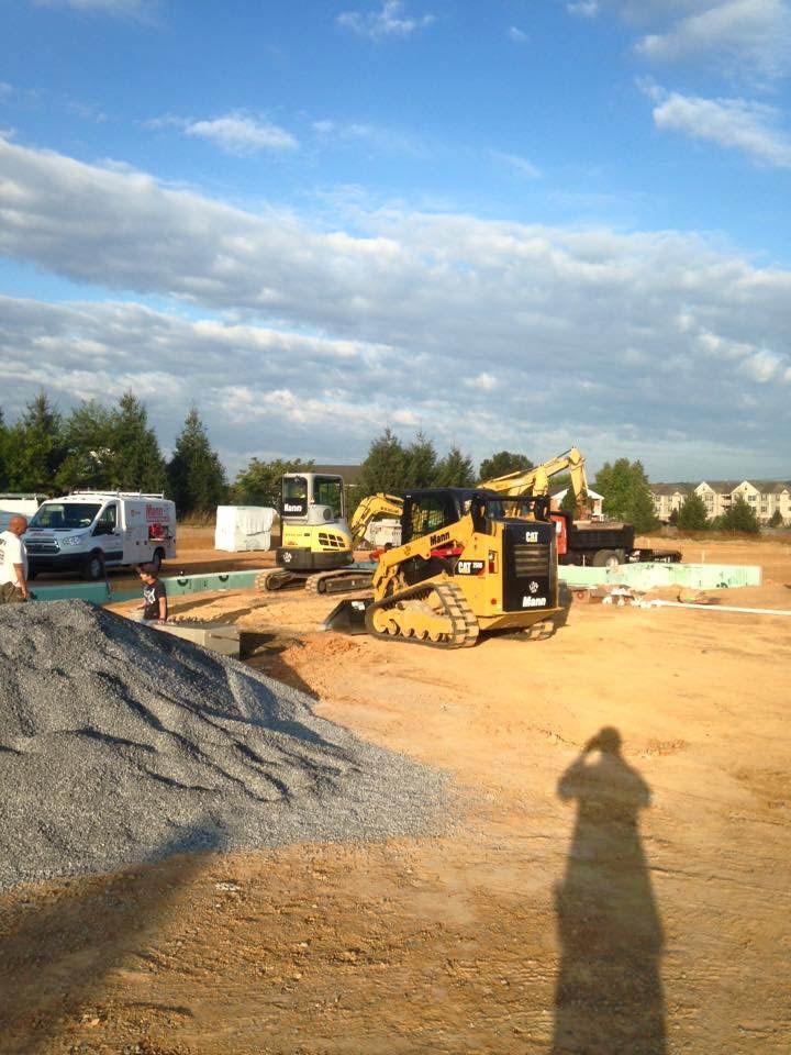 Construction site with heavy machinery on a sunny day; a pile of gravel is in the foreground.