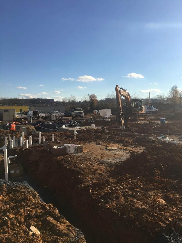 Construction site with an excavator, dirt, and various building materials under a blue sky.