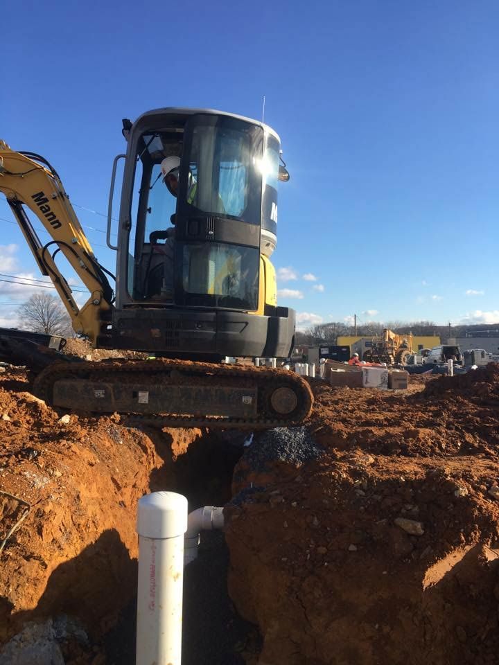 Yellow excavator digging near white PVC pipe in a construction site under a blue sky.
