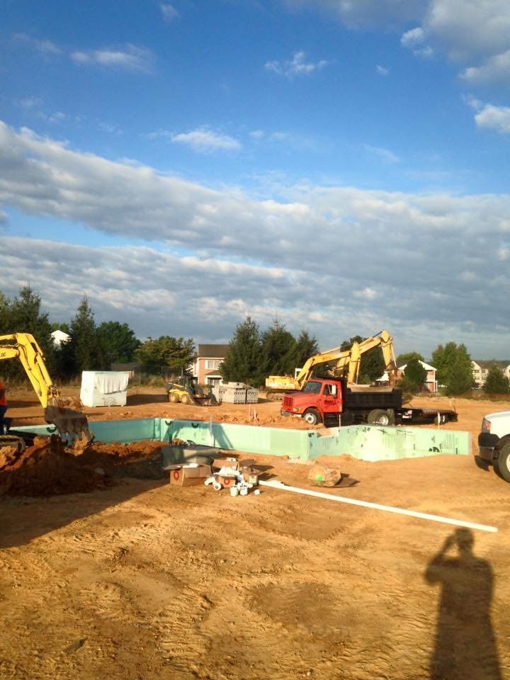 Construction site with yellow excavators and a red truck on a brown dirt lot under a blue sky.