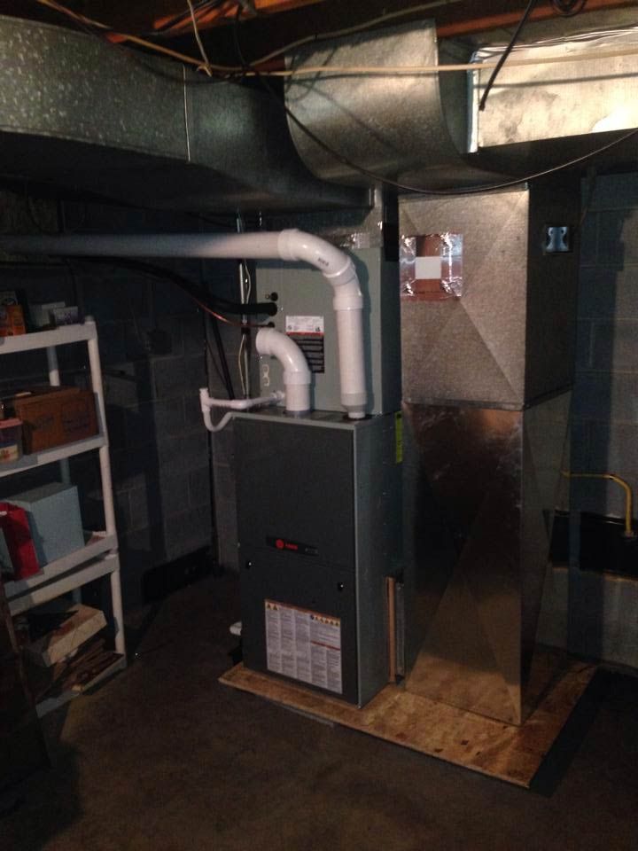 Furnace in a basement setting with ductwork, exhaust pipes, and a wooden base.