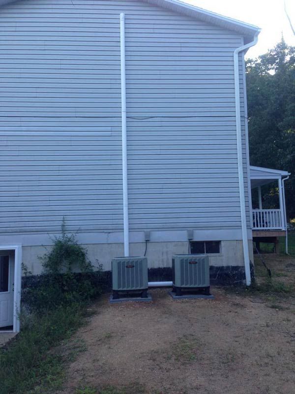 Two air conditioning units sit outside a house with white siding and a vertical pipe.