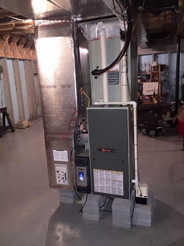 Furnace in a basement; gray metal unit on concrete blocks, connected to ductwork.