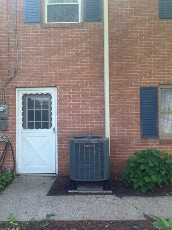 Exterior of a brick building with a white door, air conditioning unit, and blue shutters.