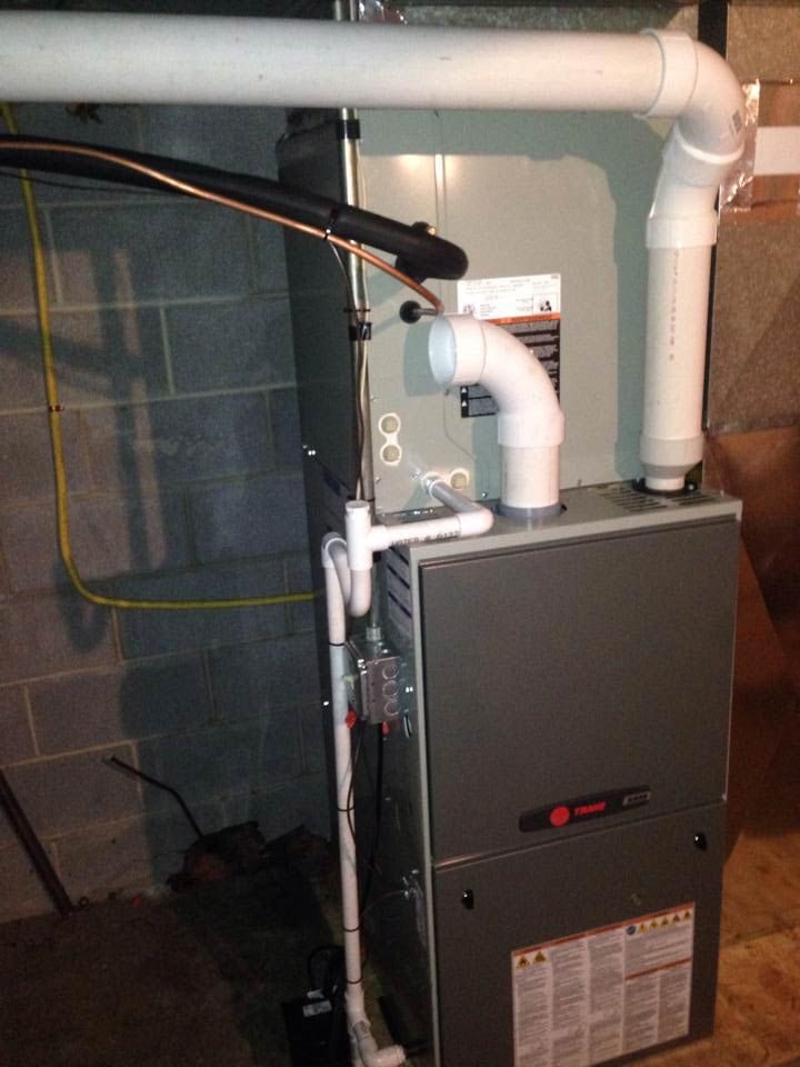 A Trane furnace in a basement setting with white PVC pipes for venting.