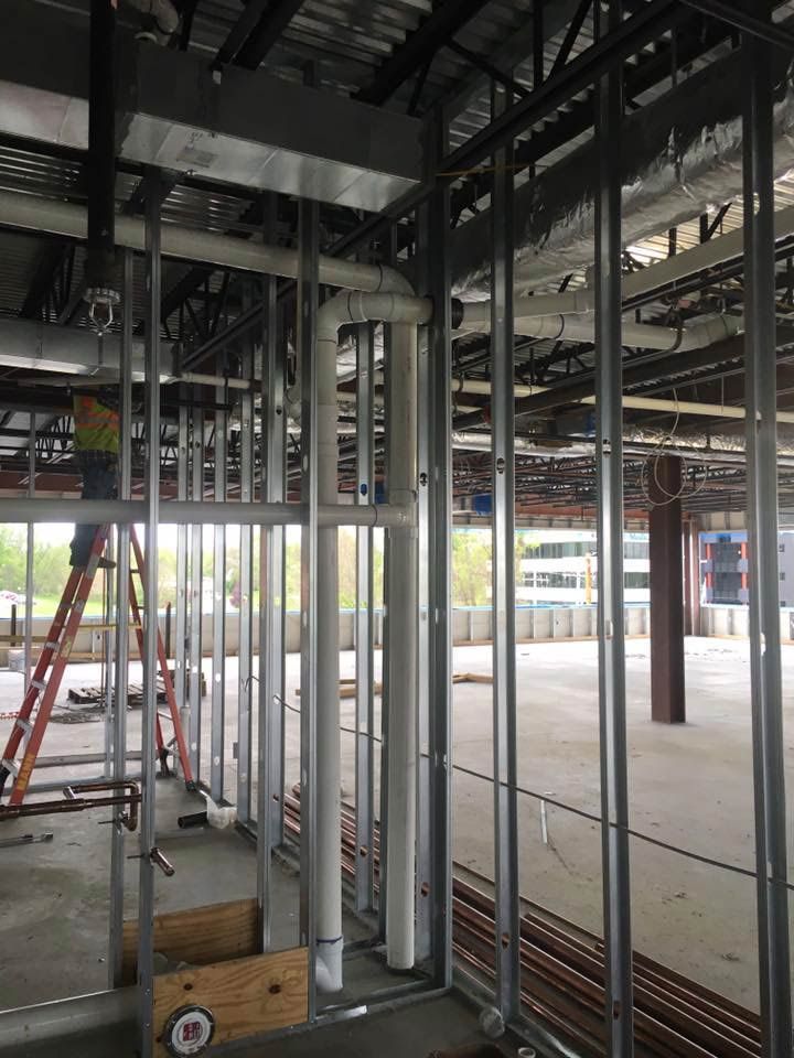 Construction site with metal framing, pipes, and a worker on a ladder.