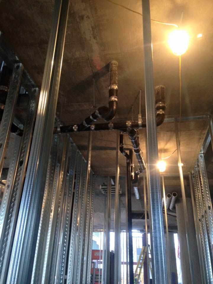 Construction site view of black plumbing pipes installed on a concrete ceiling with metal framing.