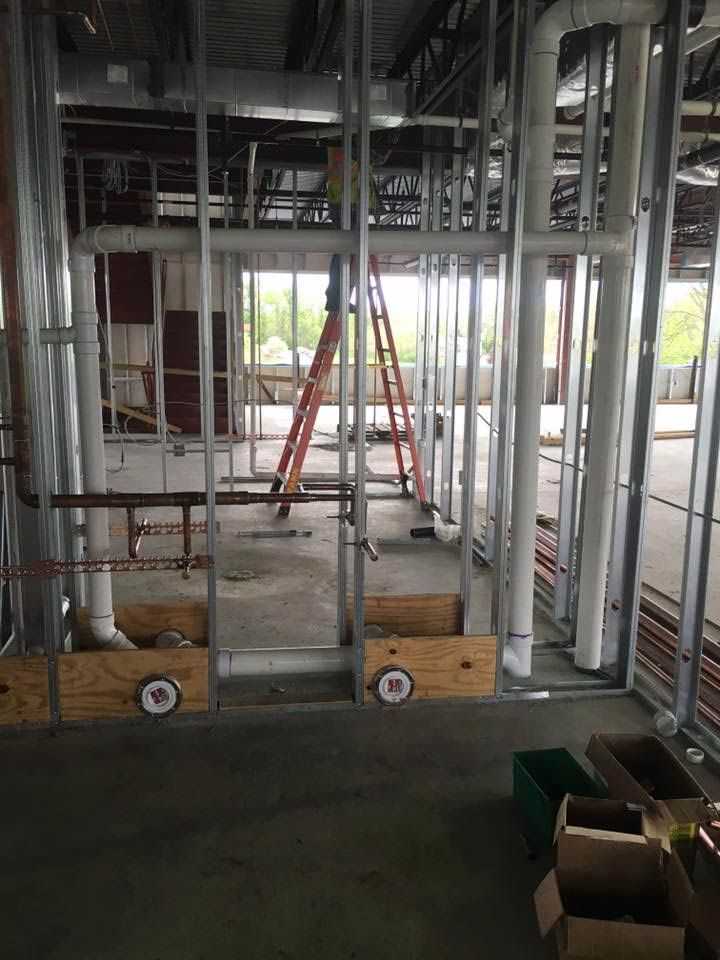 Construction site interior with exposed pipes and metal framing, orange ladder, unfinished walls.
