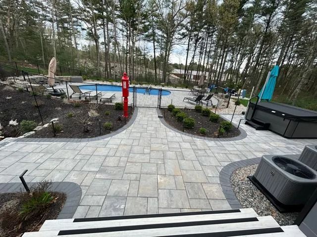 Stone patio walkway to a small pool with lounge chairs, surrounded by trees and landscaping.
