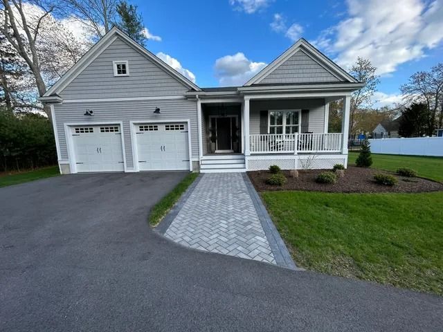 Gray house with two-car garage, front porch, and paved walkway under a blue sky