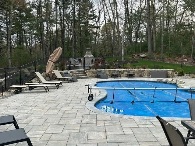 Backyard pool with blue cover, stone patio, lounge chairs, and wooded surroundings