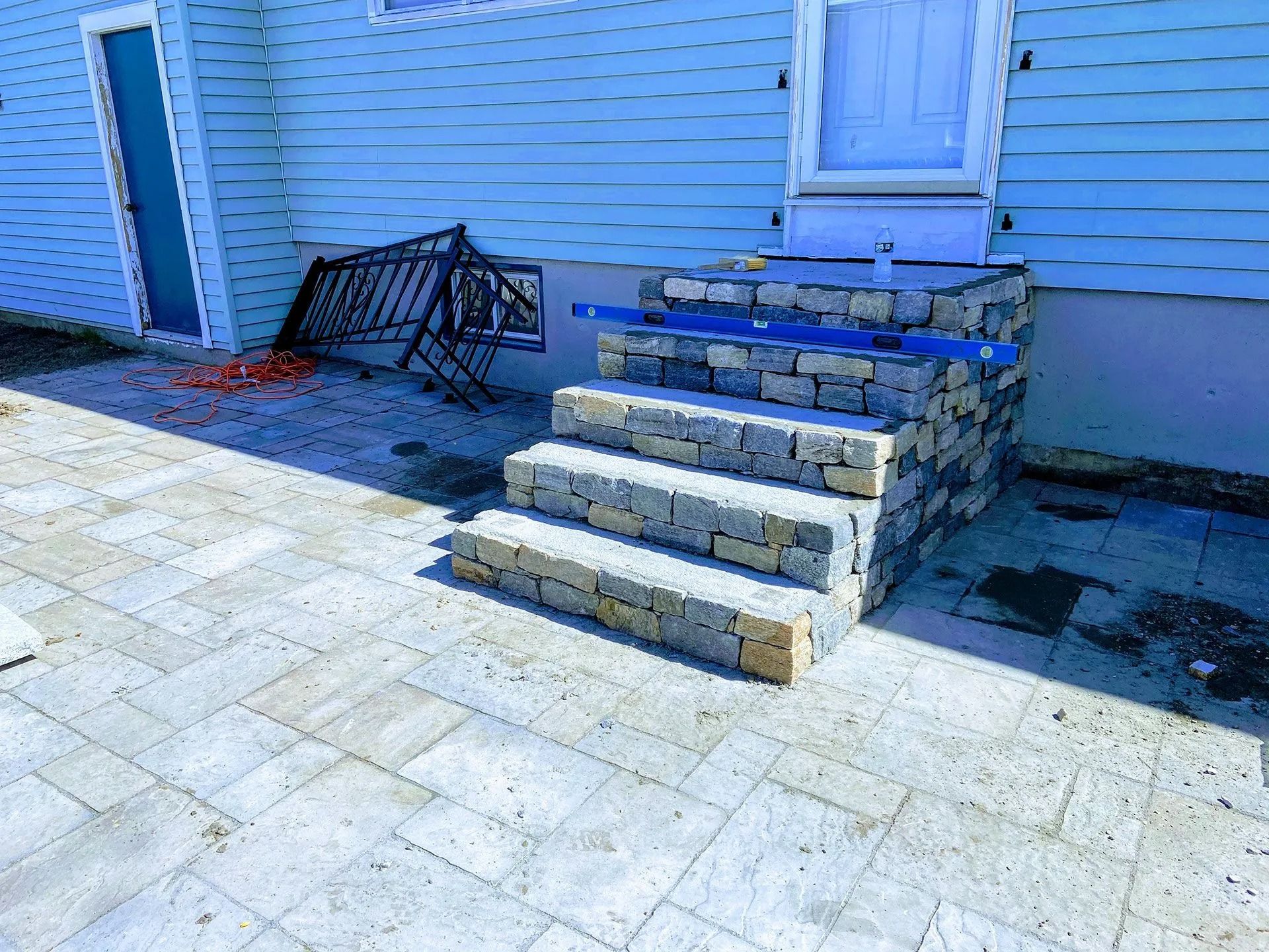 Stone steps beside a blue house, with a black metal bench and paved patio in front