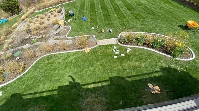 Backyard lawn with garden beds, stepping stones, and a small orange toy on the grass.