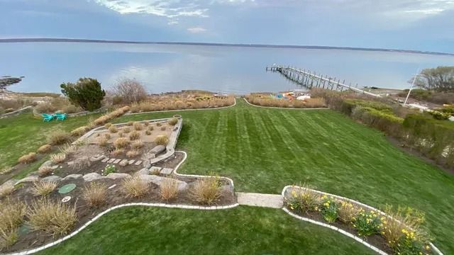 Wide green lawn with landscaped flower beds, a stone path, and a distant ocean view under cloudy skies