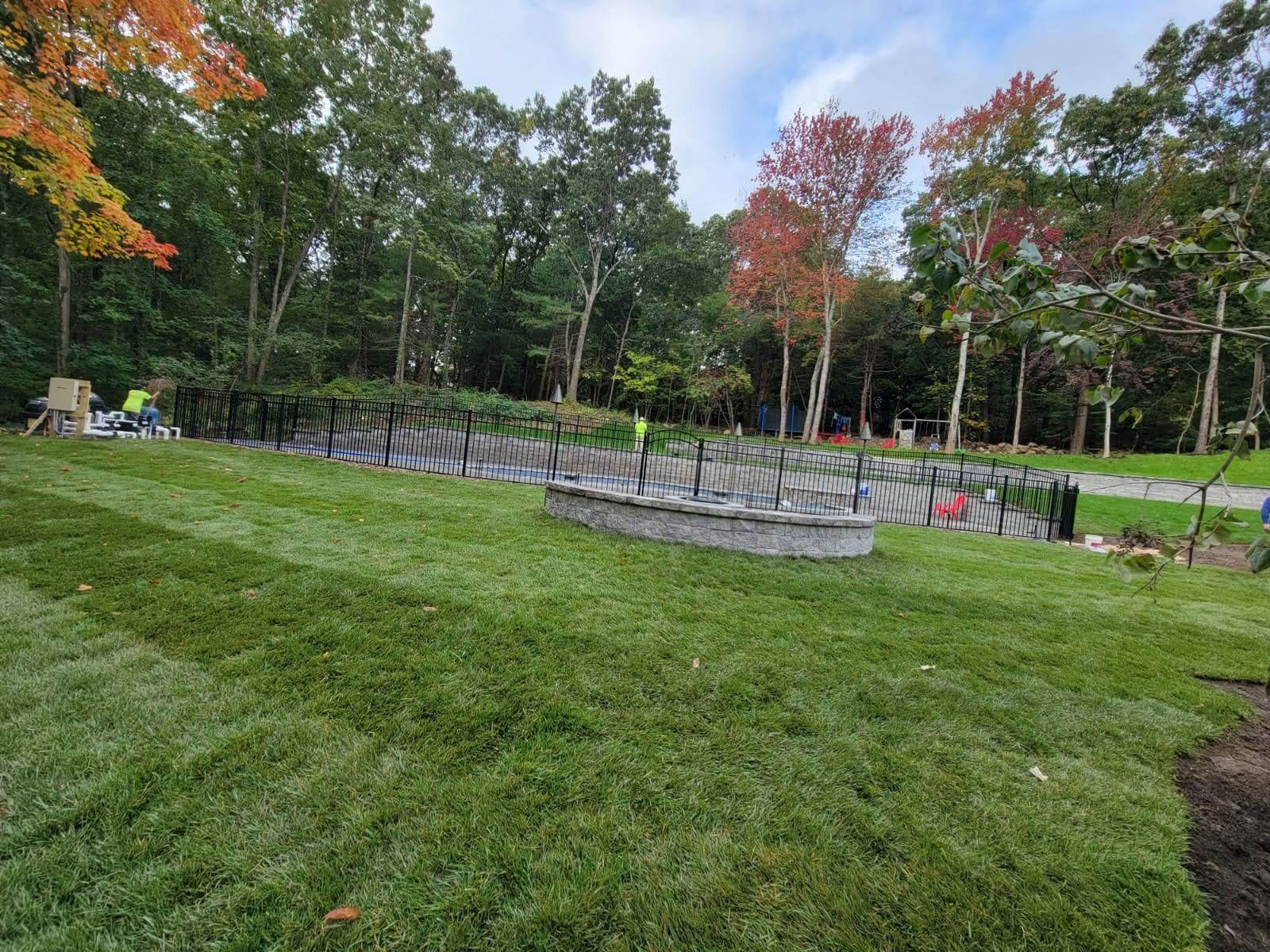 Grassy park with a circular flower bed, surrounded by trees in early autumn.