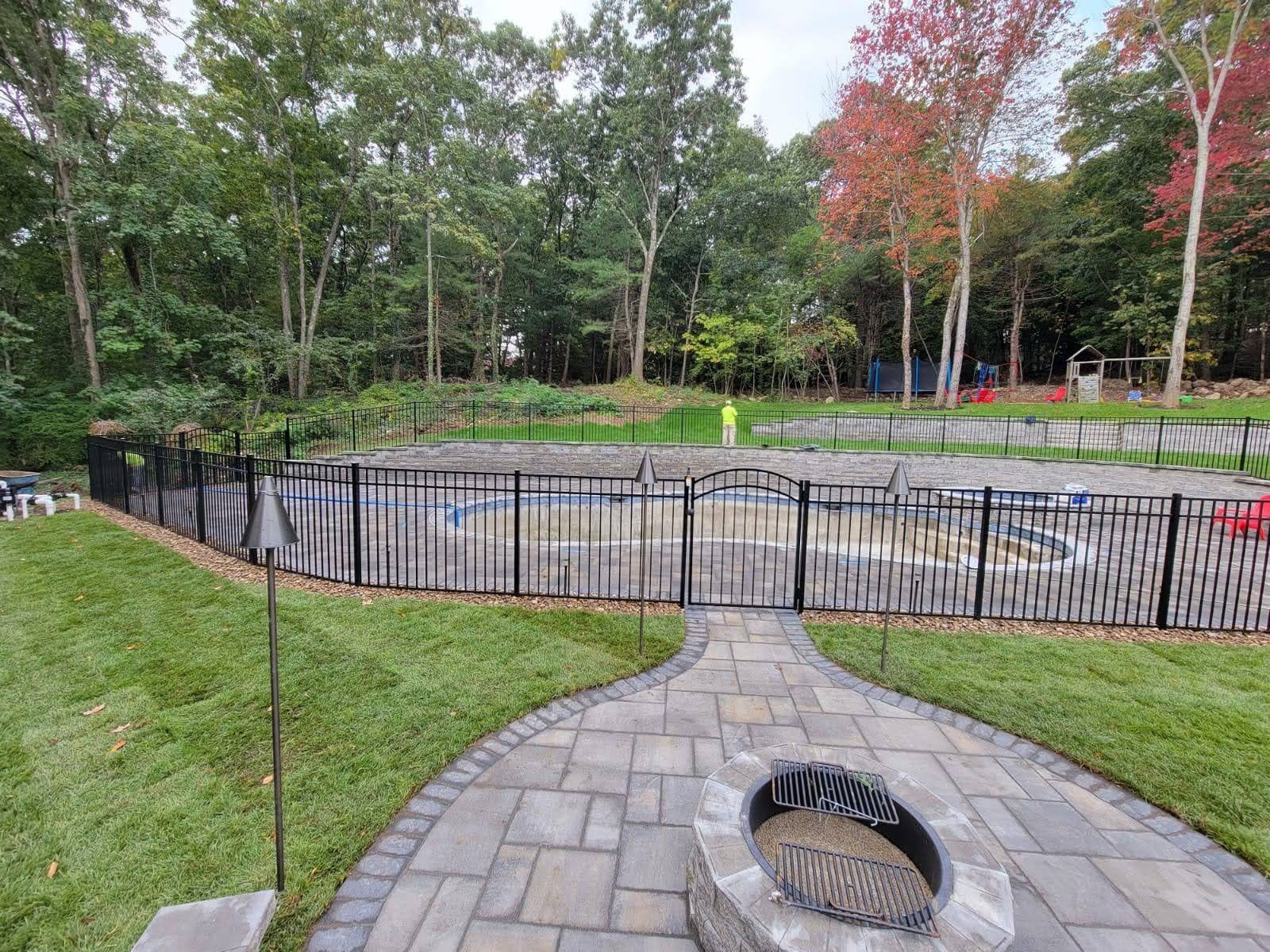 Stone patio with circular fire pit overlooking a fenced pond and trees in a park-like setting