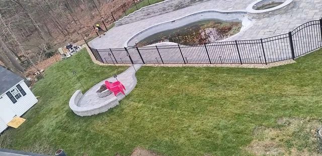 Backyard with a fenced in-ground pool, small hot tub, and red chair on the grass