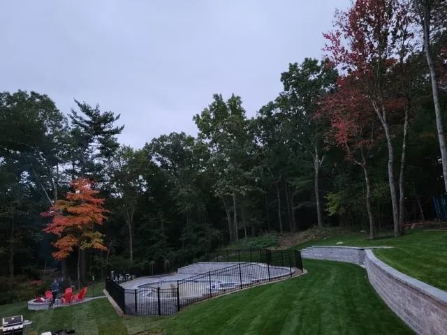 Curved pathway beside an empty fenced pool in a wooded park with autumn trees