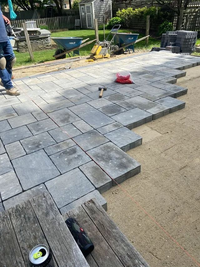 Backyard patio pavers being installed, with gray stones and a worker partly visible at left