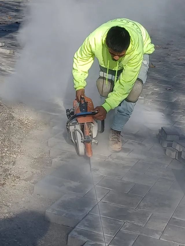 Worker in neon safety jacket cutting pavement with a power saw amid dust and smoke.