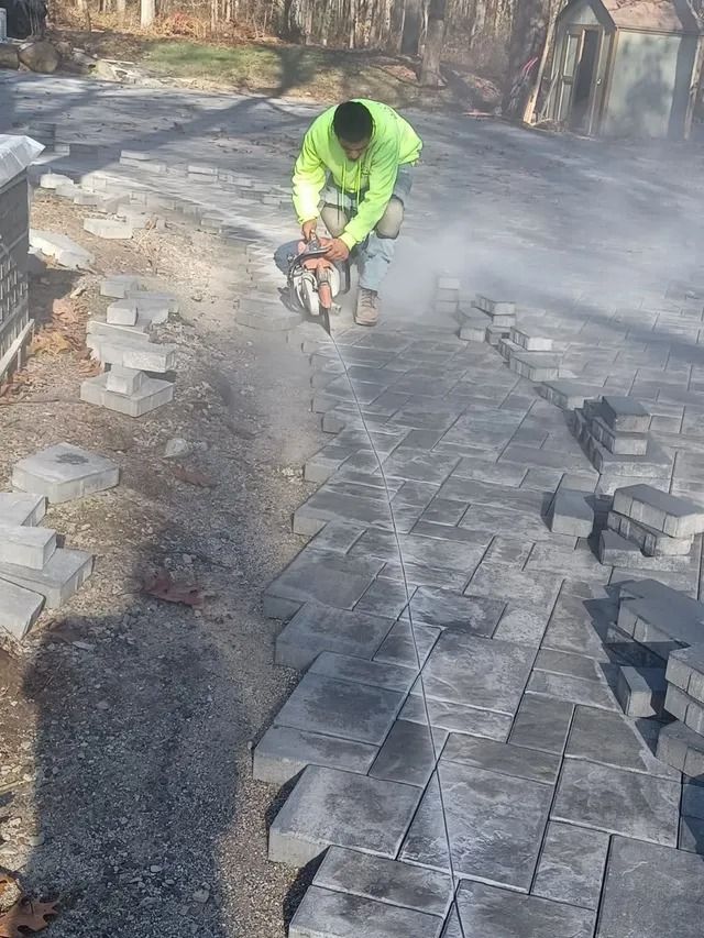 Worker in neon jacket using a jackhammer on a paved path, with dust and debris around.